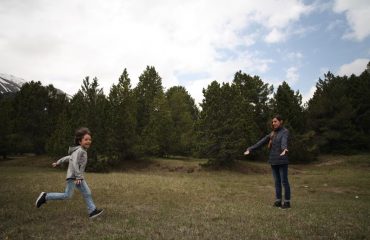 Mother and child enjoying playtime in lush Swiss landscape with trees.